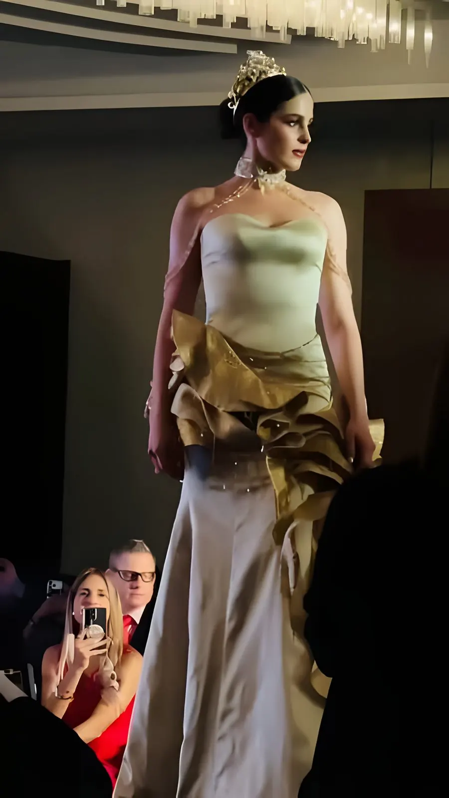 A crowned candidate walks the runway in an ivory and gold gown