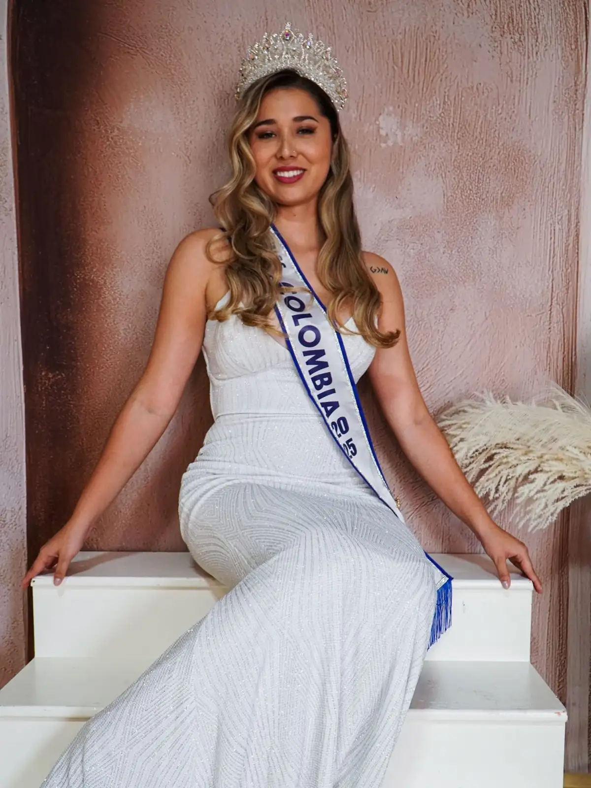 Juli, Miss Dallas Colombia 2025, seated in a white gown wearing her crown